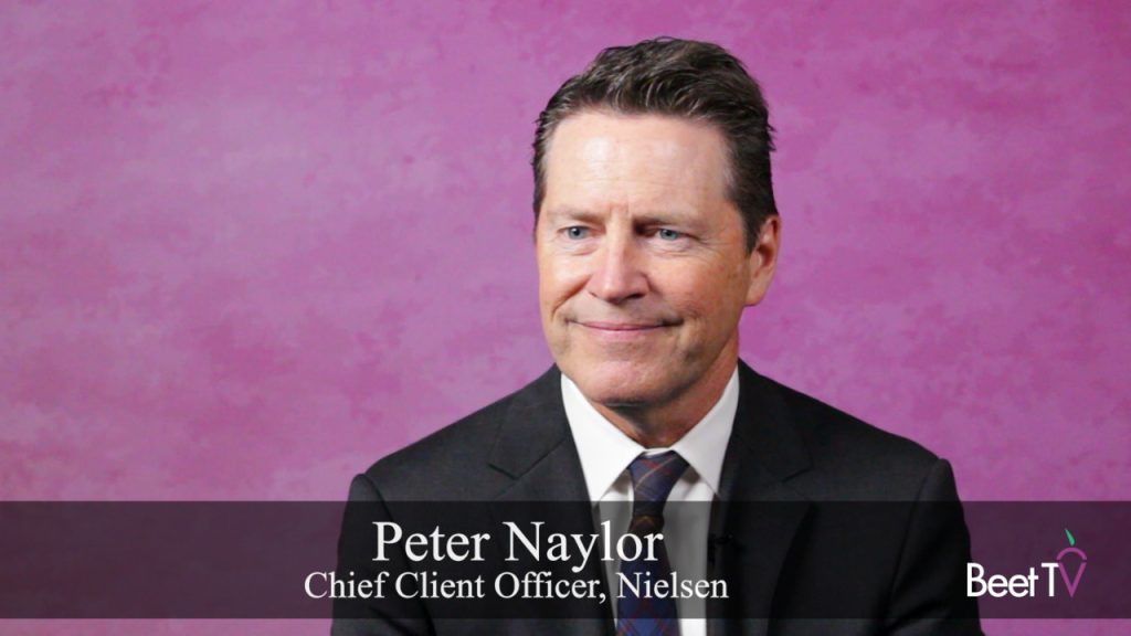 Peter Naylor speaking at a conference, with a screen displaying the Nielsen logo behind him.
