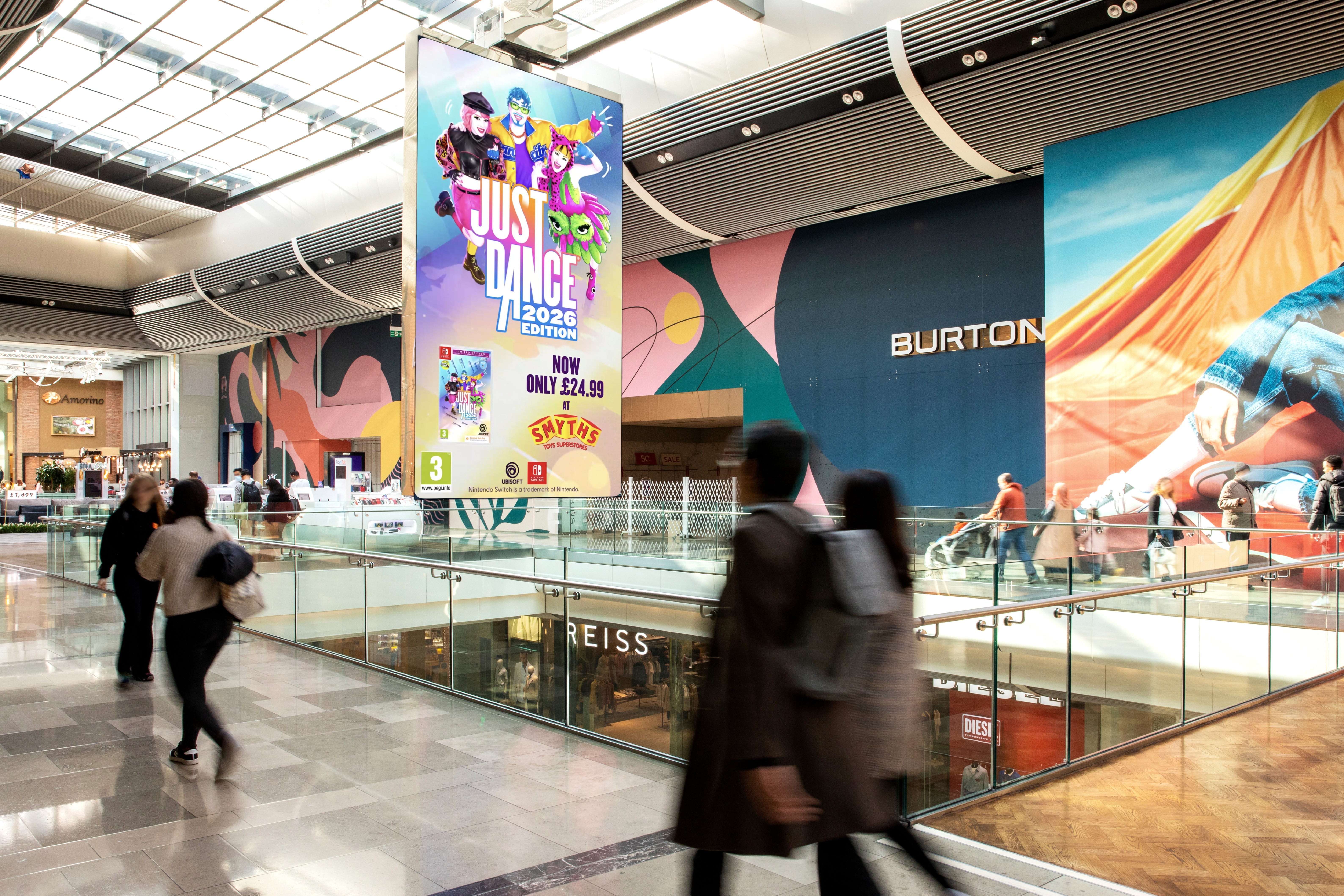 A digital billboard showing the Just Dance 2026 game cover, located near a retail store entrance.